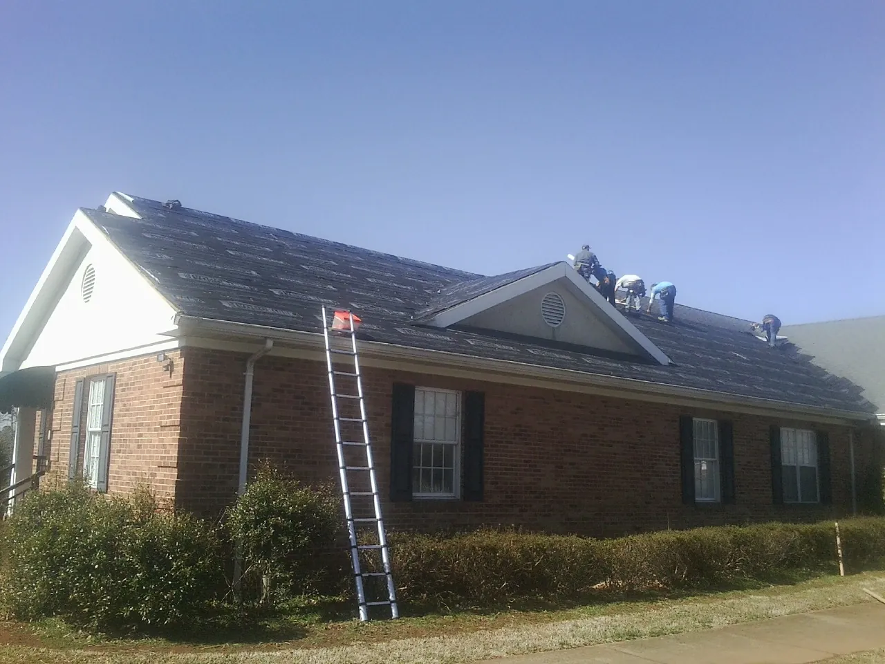 Crew tearing shingles off a brick ranch roof with a ladder set — Metal Roof Repair work by our crew in Big Bar
