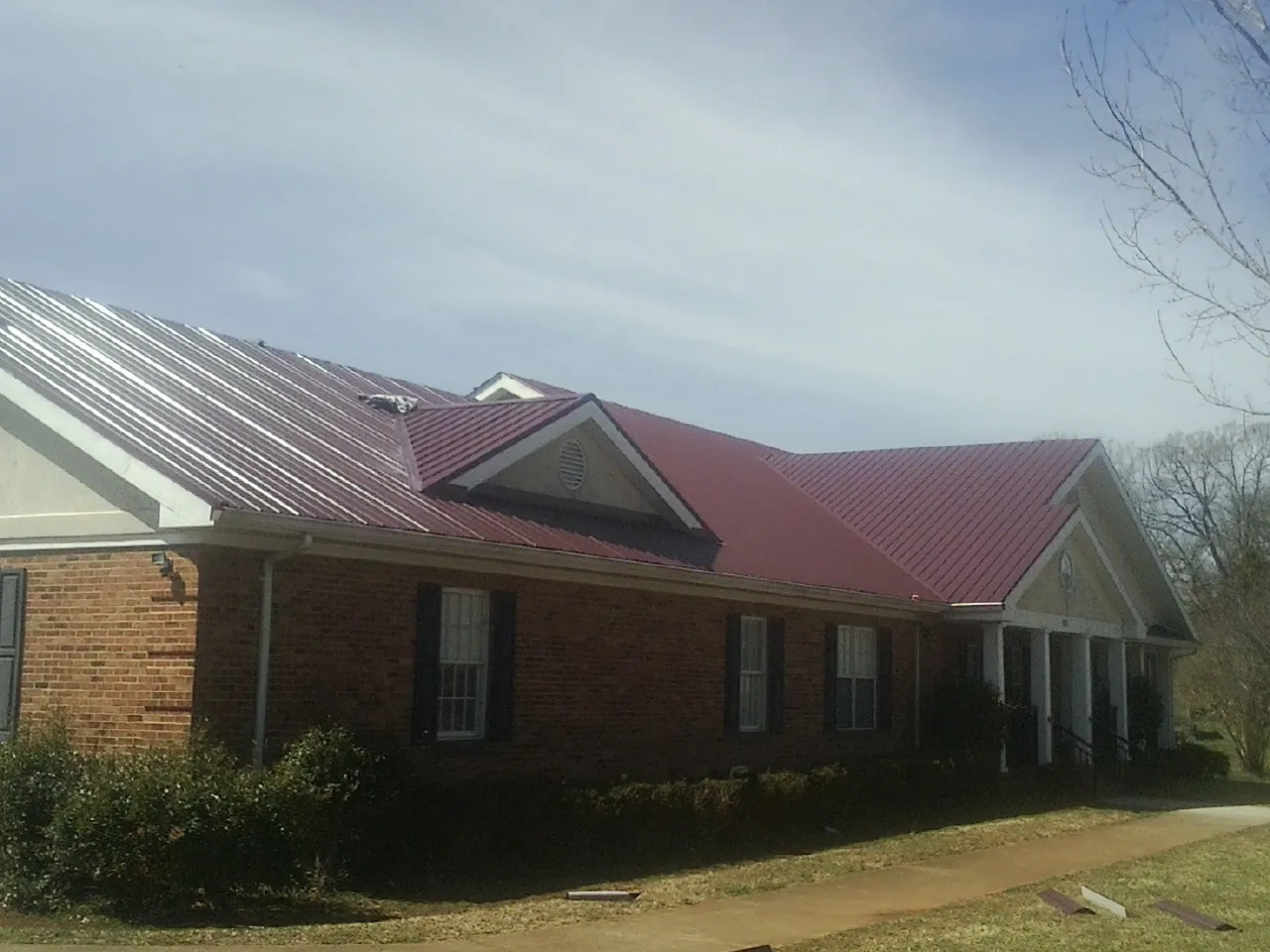 Red metal roof with gabled entries on a long brick building, from a Hail Damage Roof Repair job in Big Bar